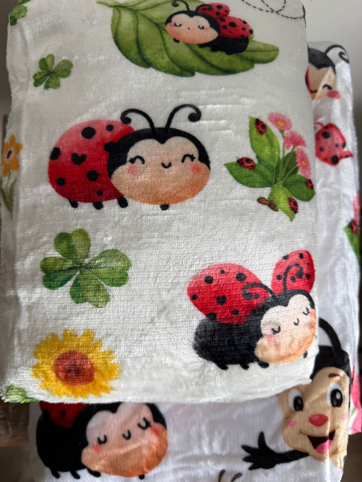 Detalle del estampado de mariquitas sonrientes, tréboles y hojas de la manta Mariquiña