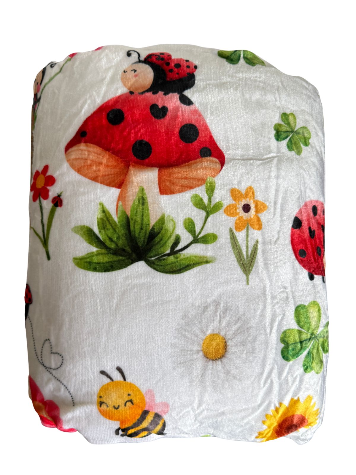 Manta de borreguillo Mariquiña enrollada con estampado de mariquita sobre una seta, margarita y abeja
