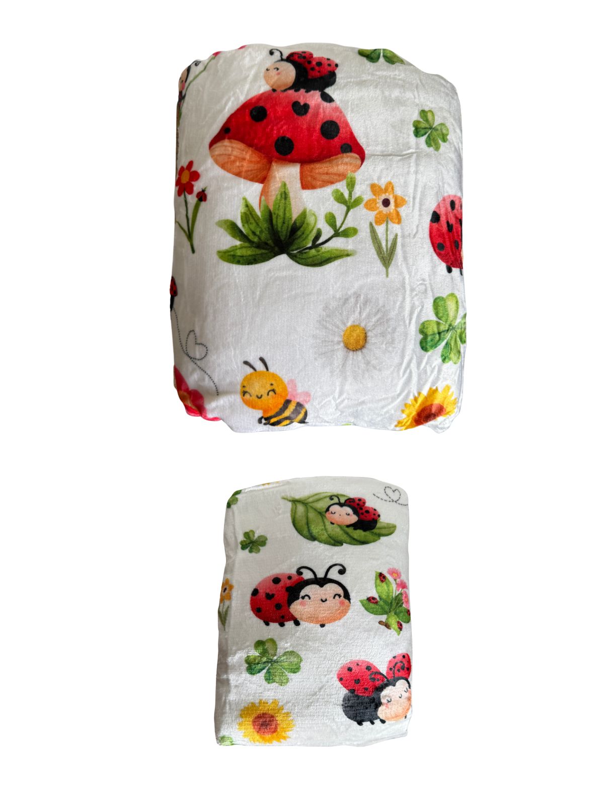 Dos mantas de borreguillo Mariquiña enrolladas, una grande y otra pequeña, con mariquitas, setas y flores